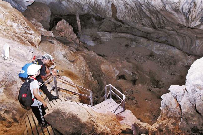 导览员彼尔维（黑衣者）向记者展示「拿督洞」天坑（sinkhole）塌陷前的原位水平线，并指「拿督洞」地质或将持续塌陷。