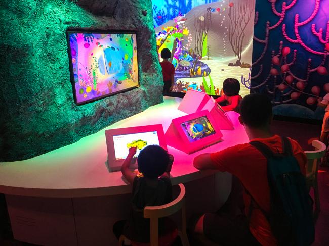 在创意创造区以平板电脑挑选自己喜爱的海洋生物，并为其上色。完成后的作品将出现在大屏幕上游动，十分有趣。