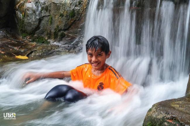 小孩在天然瀑布中戏水，享受大自然的环境及快乐。