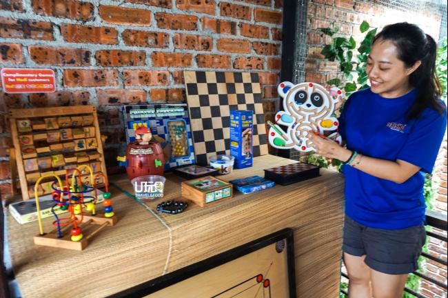游戏店助理林依幼（右）示范如何操作磁铁运笔走珠迷宫玩具，至于桌面上的游戏，一律免费供玩乐。